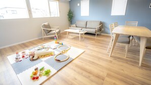 Sala de estar com sofá, cadeiras, mesa e um espaço para brincar com brinquedos e tapete.