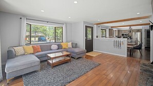 Ein modernes Wohnzimmer mit einer grauen Eckcouch, einem Holztisch und Blick auf eine Küche und einen Essbereich.