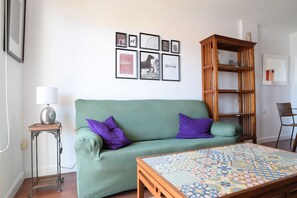 A living room with a green sofa, a patterned coffee table, a wooden bookshelf, and framed pictures on the wall.