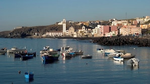 Una località costiera con barche ormeggiate lungo la riva, edifici con architetture diverse e un'imponente torre.