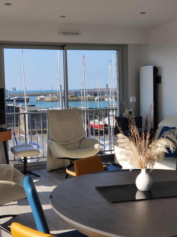 Relax in style with a panoramic marina view from this living room, featuring a round dining table, comfortable seating, and a beautiful view of the marina.