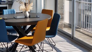 A modern dining area with a round table, blue and orange chairs, and a vase with dried plants.