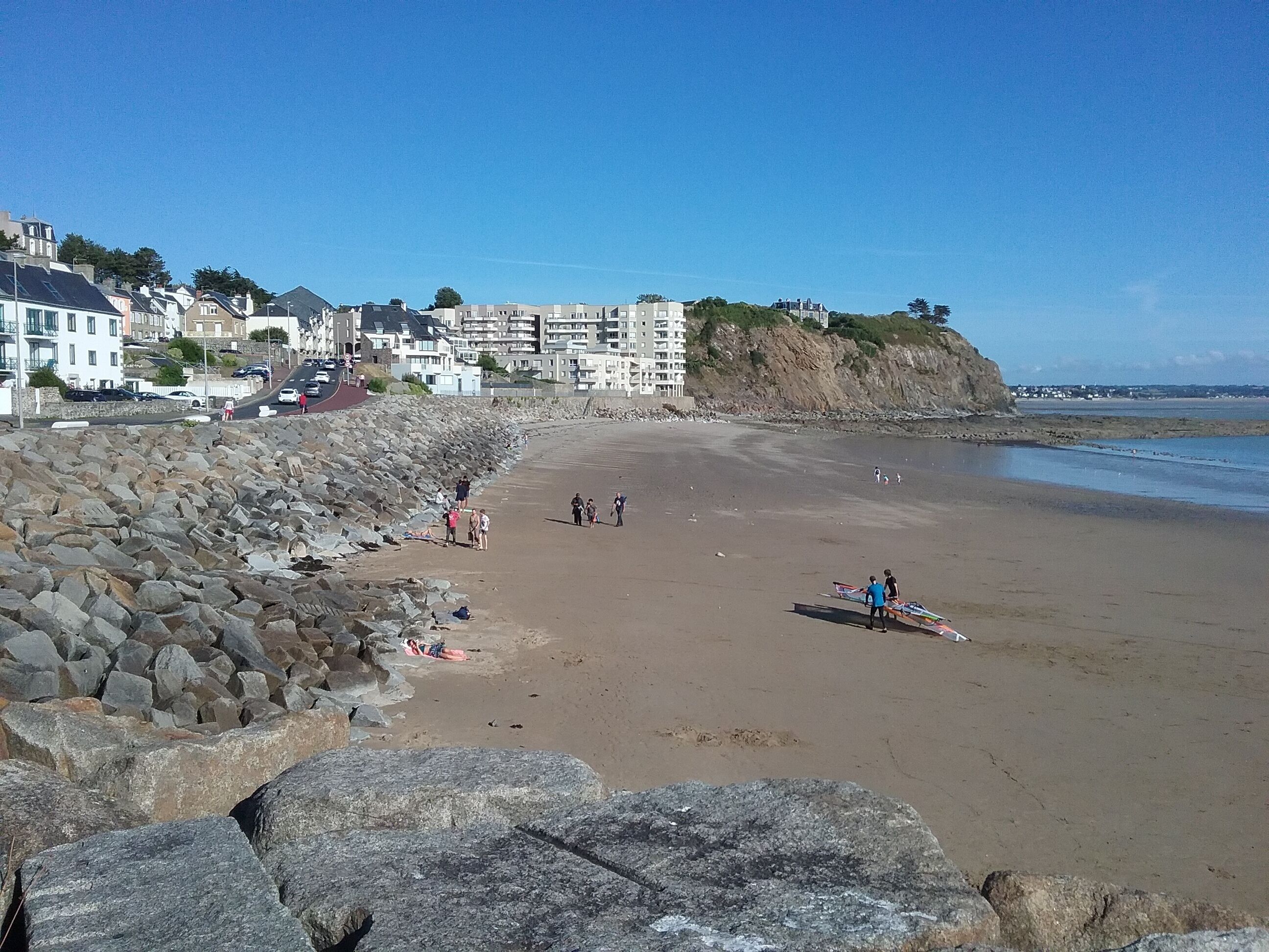 A beach with a rocky breakwater, a sandy shore, and buildings in the background.