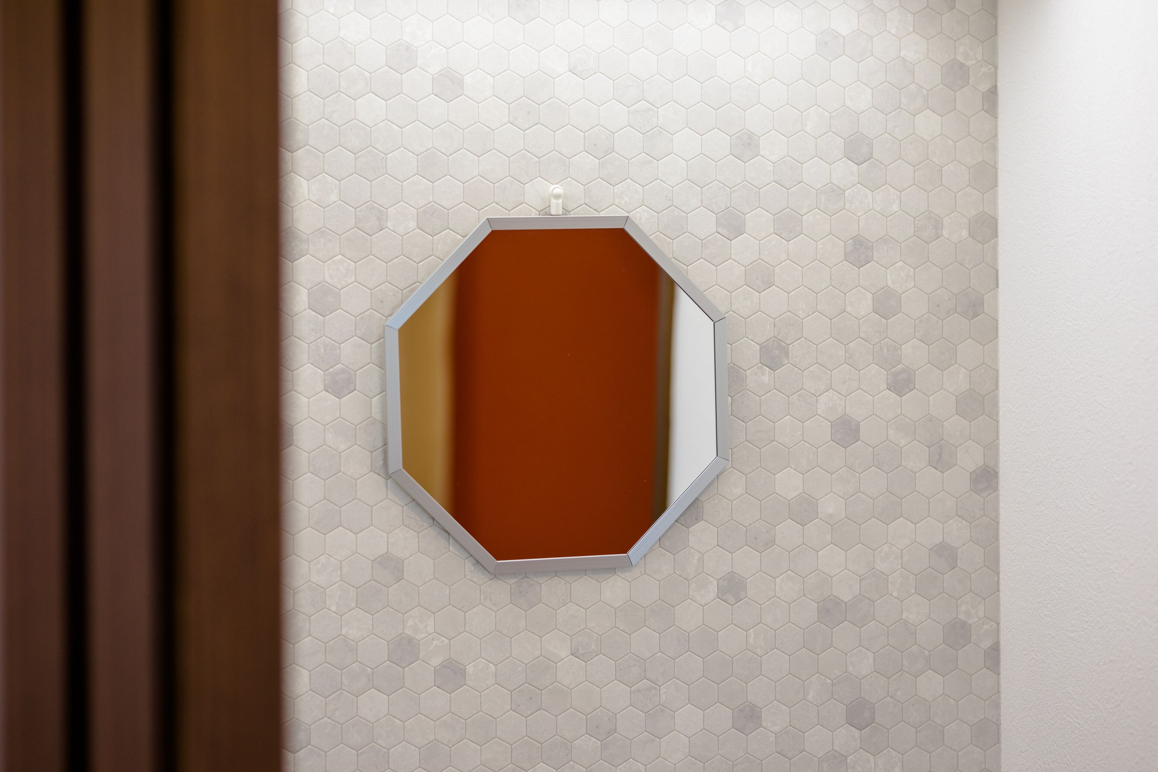 A bathroom with a hexagonal mirror and a hexagonal tile pattern on the wall.