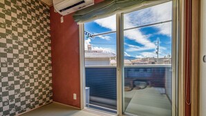 Une pièce dont un mur est orné d’un motif à carreaux, avec une porte-fenêtre coulissante donnant sur un balcon et un climatiseur fixé au plafond.