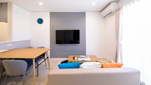 Un salon moderne avec un téléviseur à écran plat, une table à manger et un canapé agrémenté de coussins.