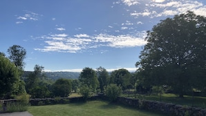 Ein grasbewachsenes Gelände mit Steinmauern und Bäumen, eine Holzterrasse und ein klarer Himmel.