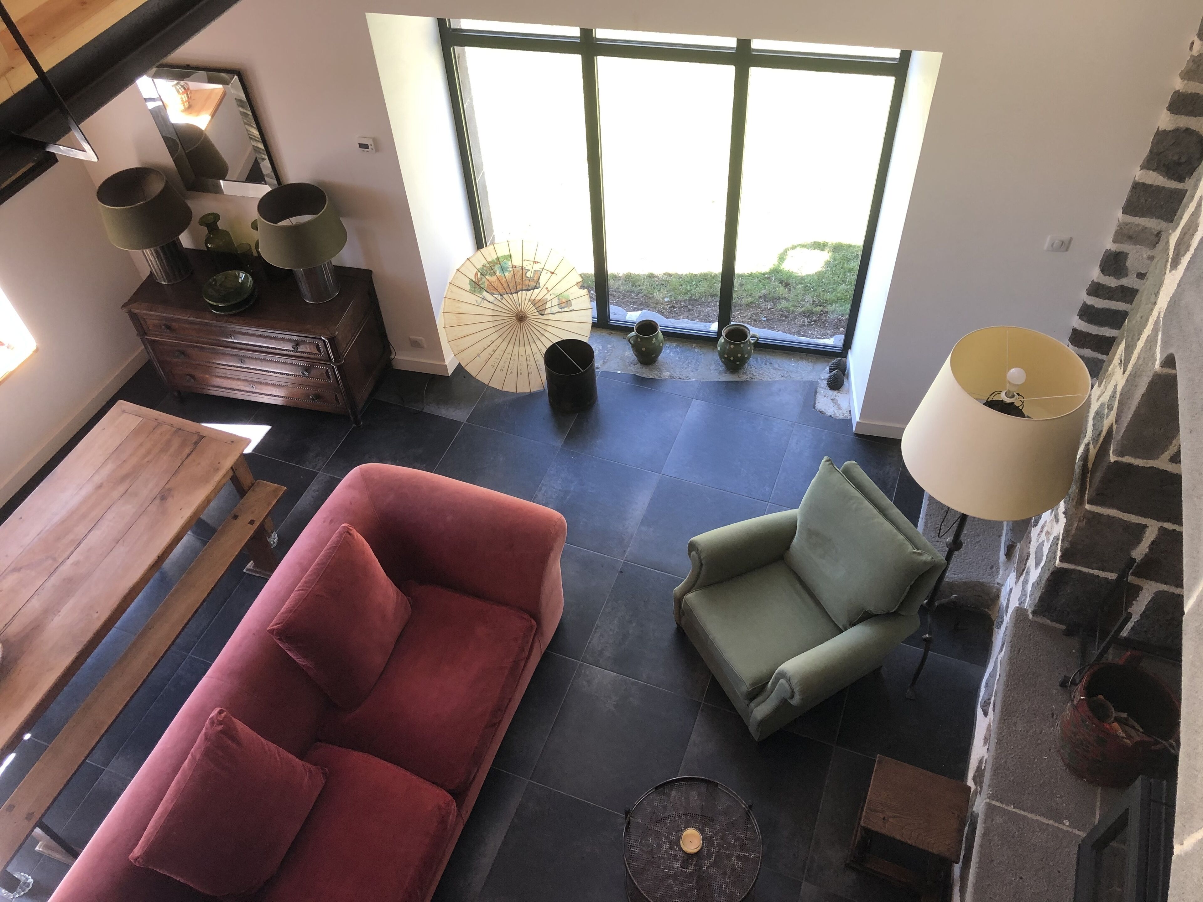 A modern living room with a red sofa, green armchair, and a wooden coffee table. There is a large window with a view of greenery outside.
