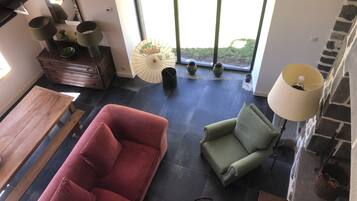 A modern living room with a red sofa, green armchair, and a wooden coffee table. There is a large window with a view of greenery outside.