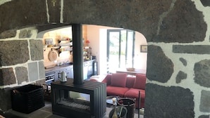 Ein Raum mit Steinsäulen, einem Kamin, einem roten Sofa und einer durch einen Bogen sichtbaren Küchenzeile.