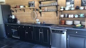 Eine moderne Küche mit schwarzen Schränken, Edelstahlgeräten, Holzregalen mit Gläsern und einem gefliesten Boden.