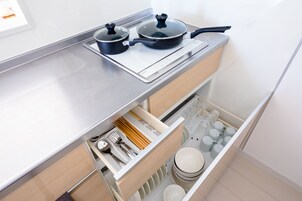 Una cocina con estufa integrada, dos ollas y un cajón con cubiertos y vajilla.