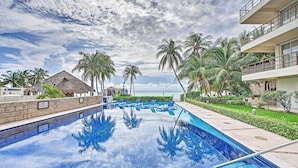 A swimming pool with lounge chairs, palm trees, and a building with balconies.