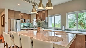 A modern kitchen with a large island, wooden cabinets, and pendant lighting.