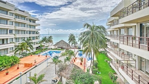 A resort with multiple balconies, a swimming pool, and a view of the ocean.