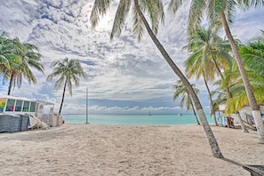 A beach with palm trees, a beach hut, and a sailboat in the distance.