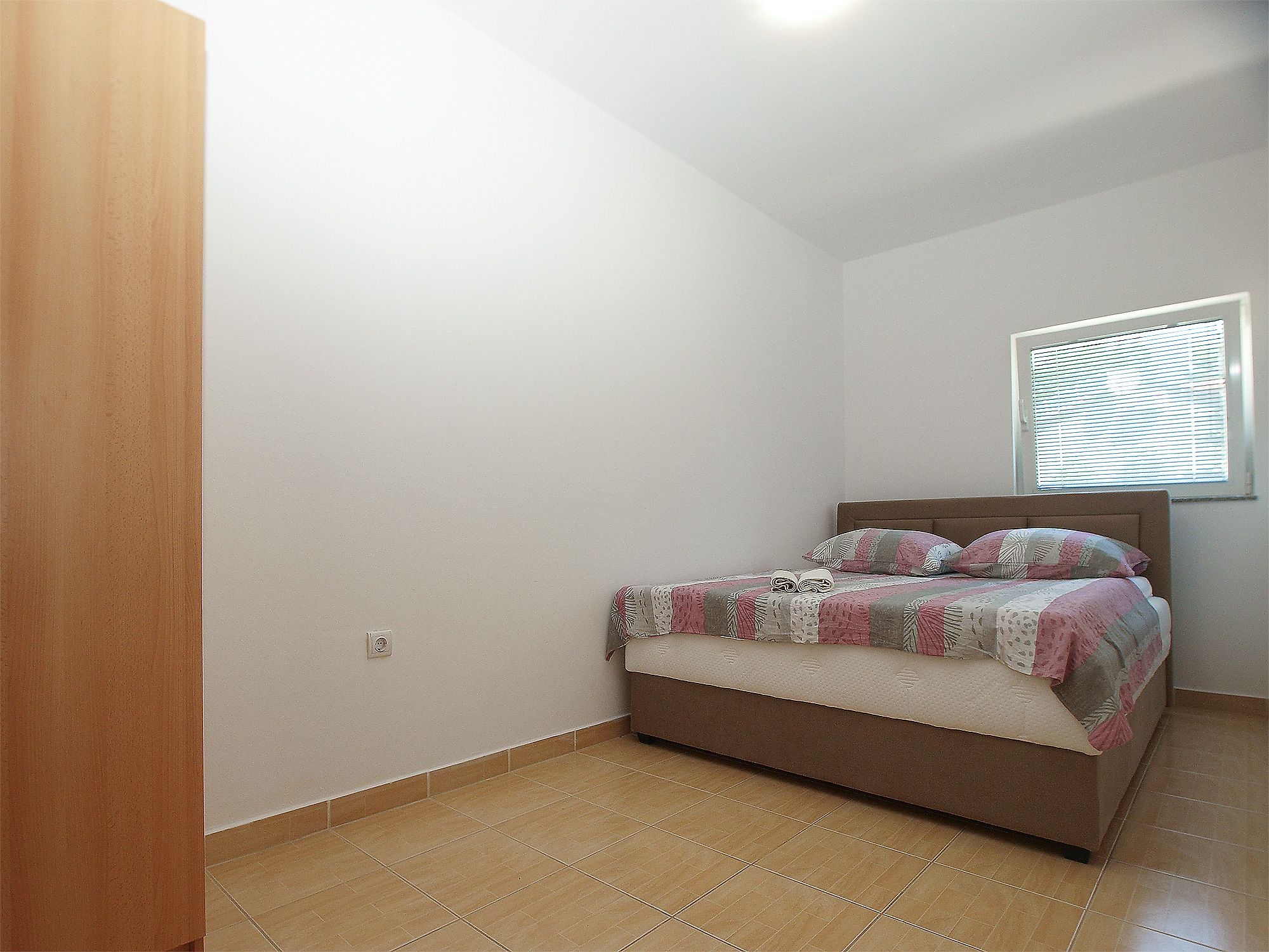 Un dormitorio con una cama, una ventana con persianas y una puerta.