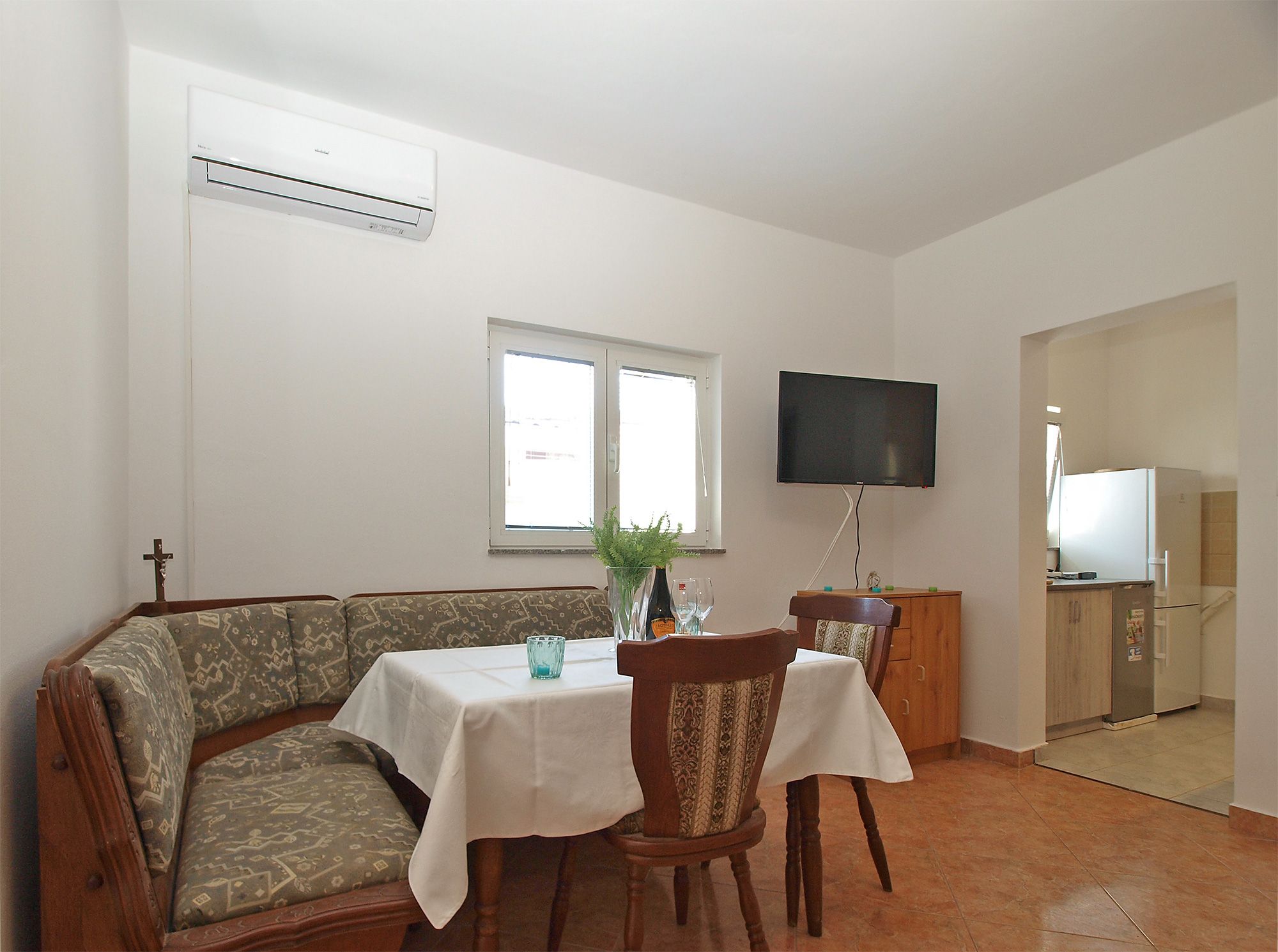 A dining area with a table, chairs, a television, and a kitchen area in the background.