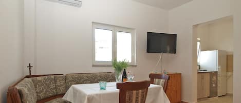 A dining area with a table, chairs, a sofa, a TV, and a kitchen area.