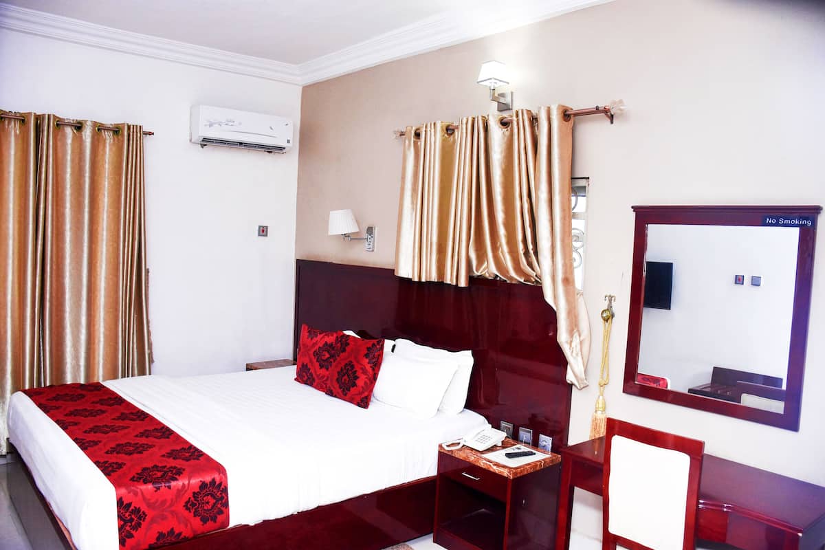 Une chambre d’hôtel avec un grand lit, une table de chevet avec un téléphone, un miroir et un panneau indiquant « Il est interdit de fumer ».