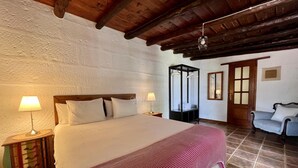 Un dormitorio con una cama grande, dos lámparas de noche, un cabecero de madera, una colcha a rayas rojas, un armario de madera y una silla.
