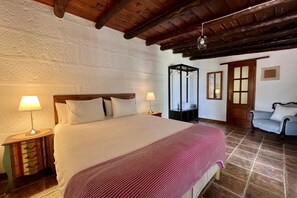 Quarto com uma cama grande, duas luminárias de cabeceira, um painel de madeira, um cobertor listrado de vermelho e madeira, um armário e uma cadeira.