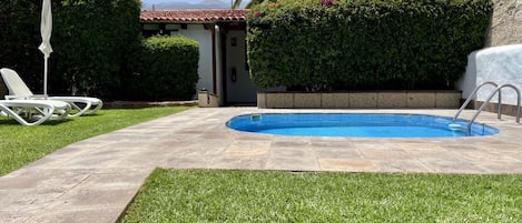A swimming pool with a tiled deck, a lounge chair, and a palm tree.