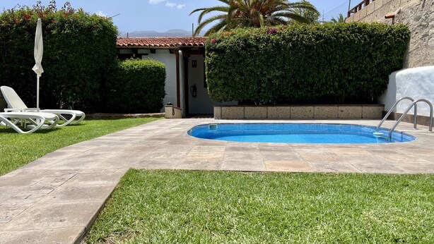 Una piscina con borde de baldosas, una silla de descanso y una palmera.