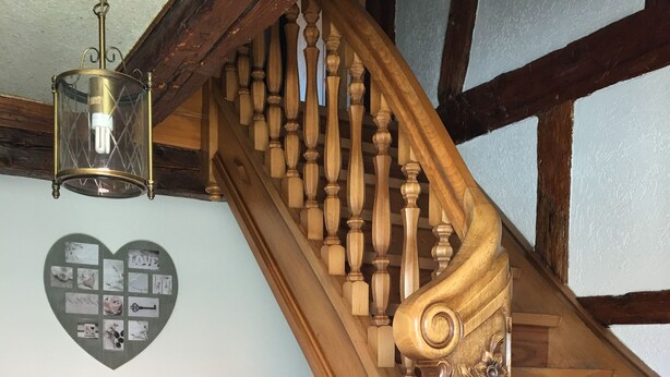 A wooden staircase with intricate carvings, a heart-shaped photo collage on the wall, and a vintage chair with a cushion.