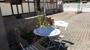 A patio area with a round metal table and two wooden chairs, surrounded by potted plants and flowers.
