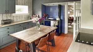 A kitchen with a wooden table, two chairs, a vase with flowers, and a blue tiled backsplash. - Ochil Cottage In Bannockburn, Close to Stirling (Stirling)