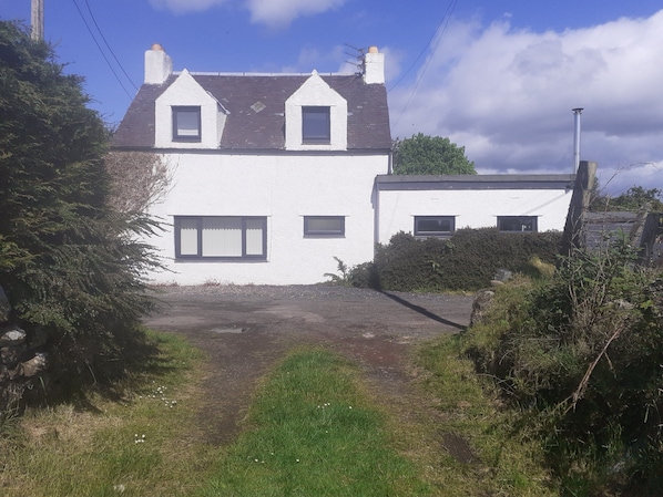 A white two-story house with a sloped roof, two chimneys, and a front yard with a dirt path leading to the entrance. - Ochil Cottage In Bannockburn, Close to Stirling (Stirling)