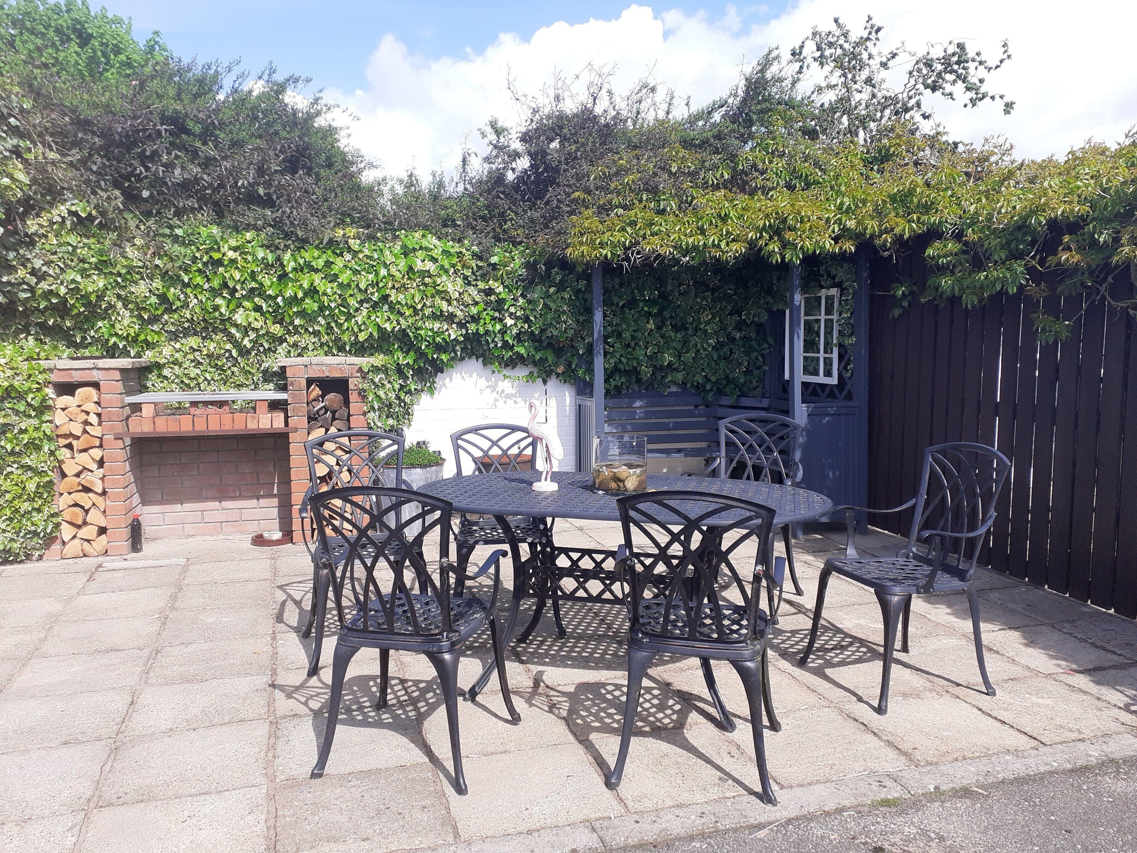 An outdoor patio with a brick fireplace, metal chairs, and a table.