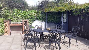 An outdoor patio with a brick fireplace, metal chairs, and a table.