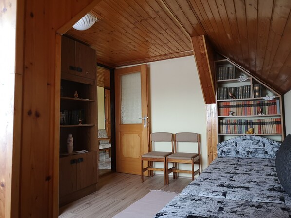 A cozy room with wooden walls and ceiling, a bed with a patterned cover, a bookshelf, and two chairs. - Szabó Vendégház (Siklós)