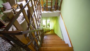 Una escalera de madera con barandilla que lleva a un rellano en el segundo piso, con una ventana y una silla.