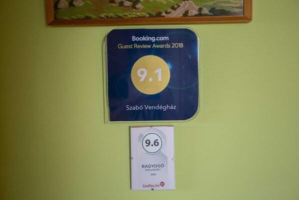 Dos premios en una pared: "Booking.com Guest Review Awards 2018" con una puntuación de 9.1 para Szabó Vendegház, y "RAGYOGÓ SZALLASHELY 2019" con una puntuación de 9.6 para Szallas.hu.