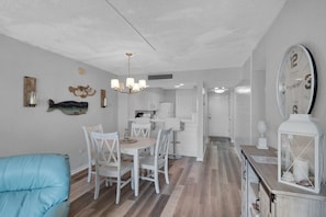 A modern kitchen with white cabinets, a dining area with white chairs, and a large wall clock.