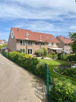 Ein Wohngebäude mit rotem Ziegeldach, zahlreichen Fenstern und einem gepflegten Garten mit grüner Umzäunung.