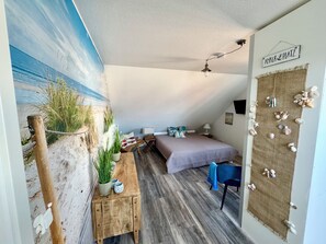 Ein gemütliches Schlafzimmer mit Bett, Schreibtisch und Stuhl. Ein Bild hängt an der Wand, und ein Schild zeigt „Anker & Platz“.