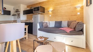 Un espace de vie compact comprenant un coin cuisine, un canapé avec des coussins, une petite table et une chaise.