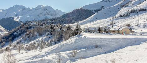 A snow-covered mountain landscape with a small cluster of buildings, likely a resort or lodge, in the foreground.