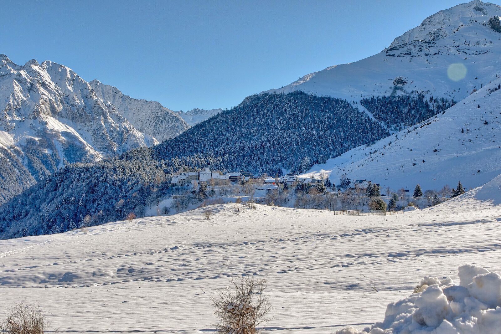 Un paisaje montañoso cubierto de nieve con un pequeño conjunto de edificios, probablemente un complejo turístico o una cabaña, ubicados entre los árboles.