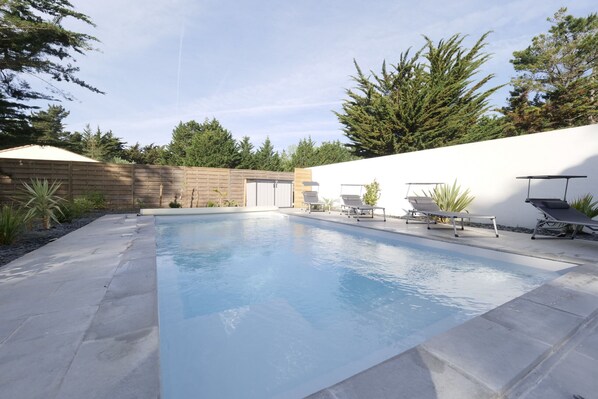 Una piscina rectangular con una cerca de madera y una pared blanca al fondo.