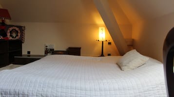 A bedroom with a large bed, a bedside table, a lamp, and a wall-mounted shelf.