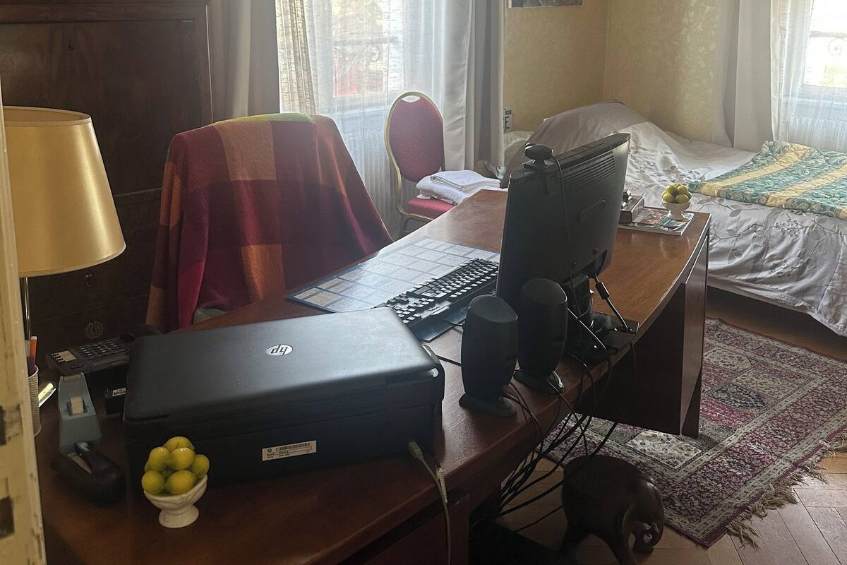 Ein Schlafzimmer mit einem Bett, einem Schreibtisch mit Computer, einer Lampe und einem kleinen Tisch mit Obstschale.