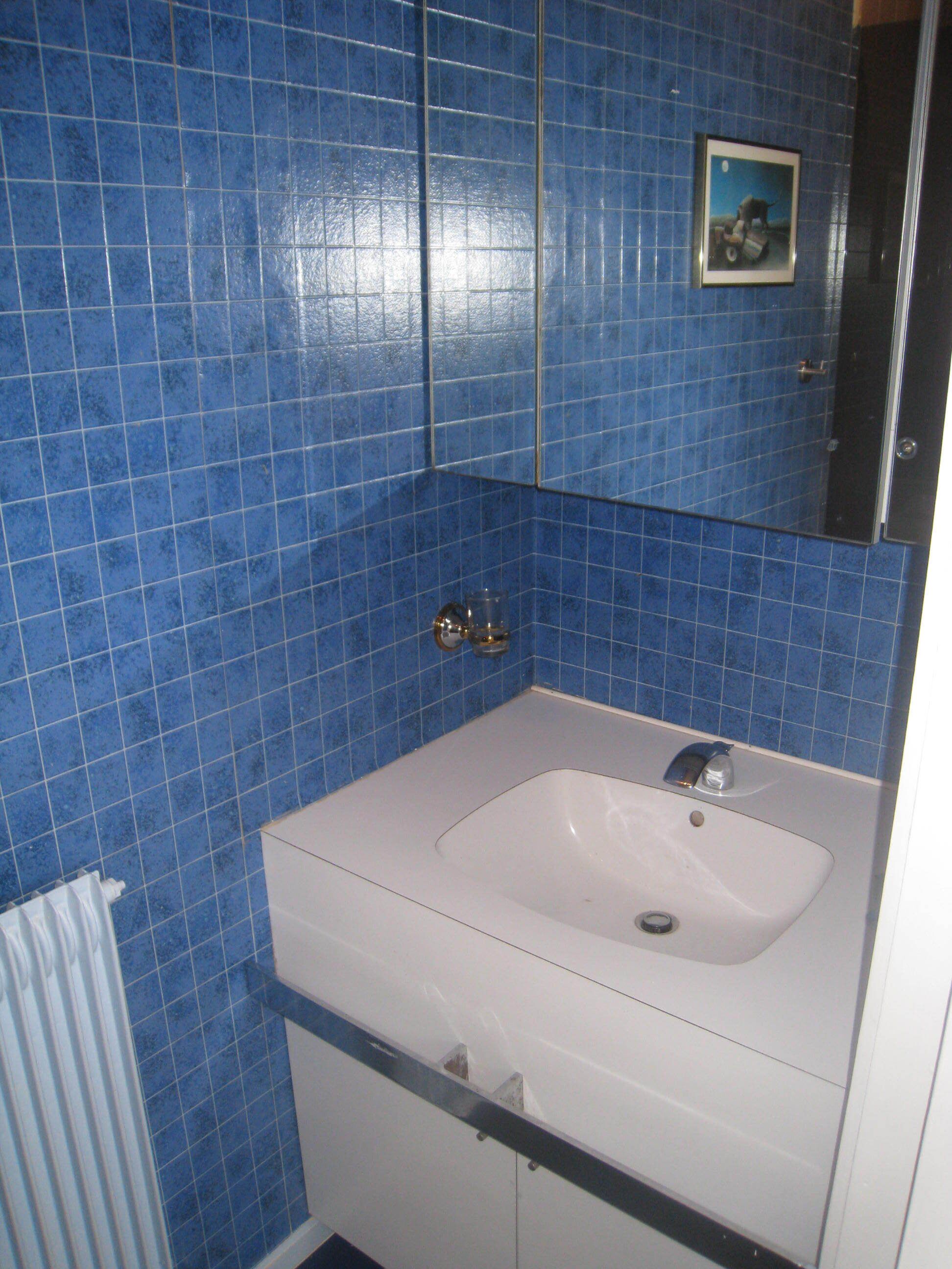 Une salle de bain avec des carreaux bleus, un lavabo blanc et un petit tableau encadré accroché au mur.
