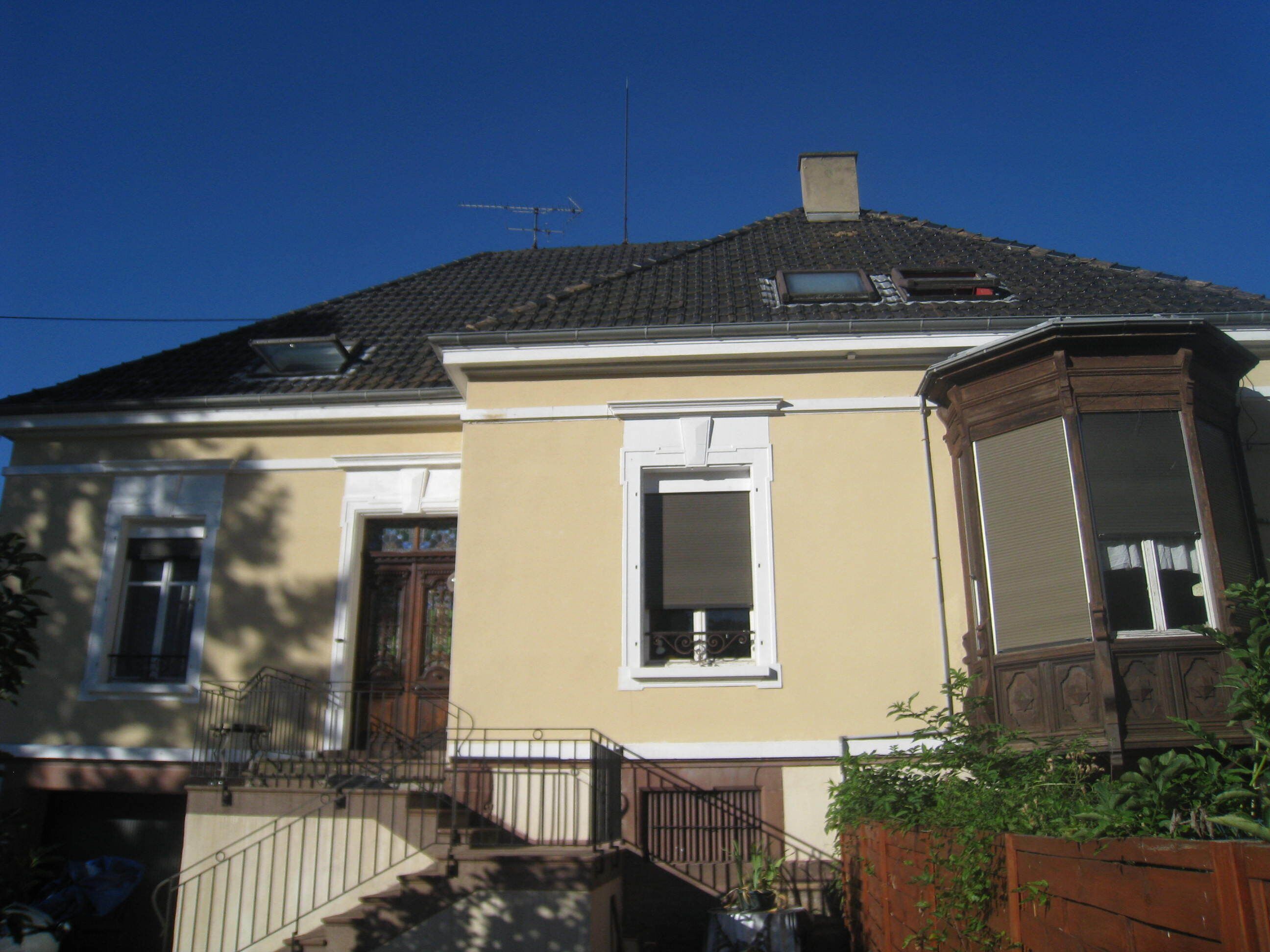 A two-story building with a beige facade, a wooden door, and a window with a white frame.