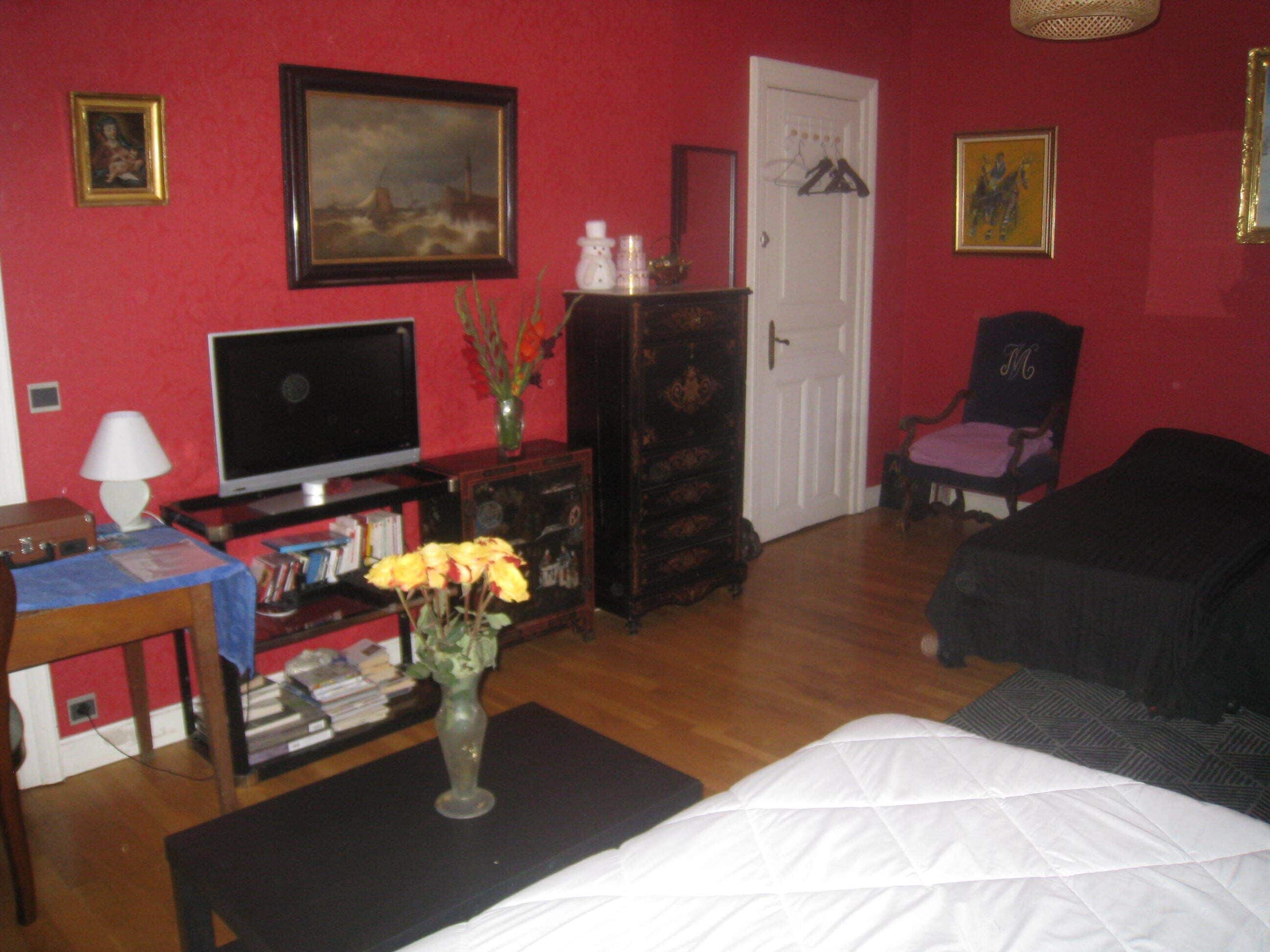 A room with a bed, a TV, a dresser, a chair, and a vase with flowers.