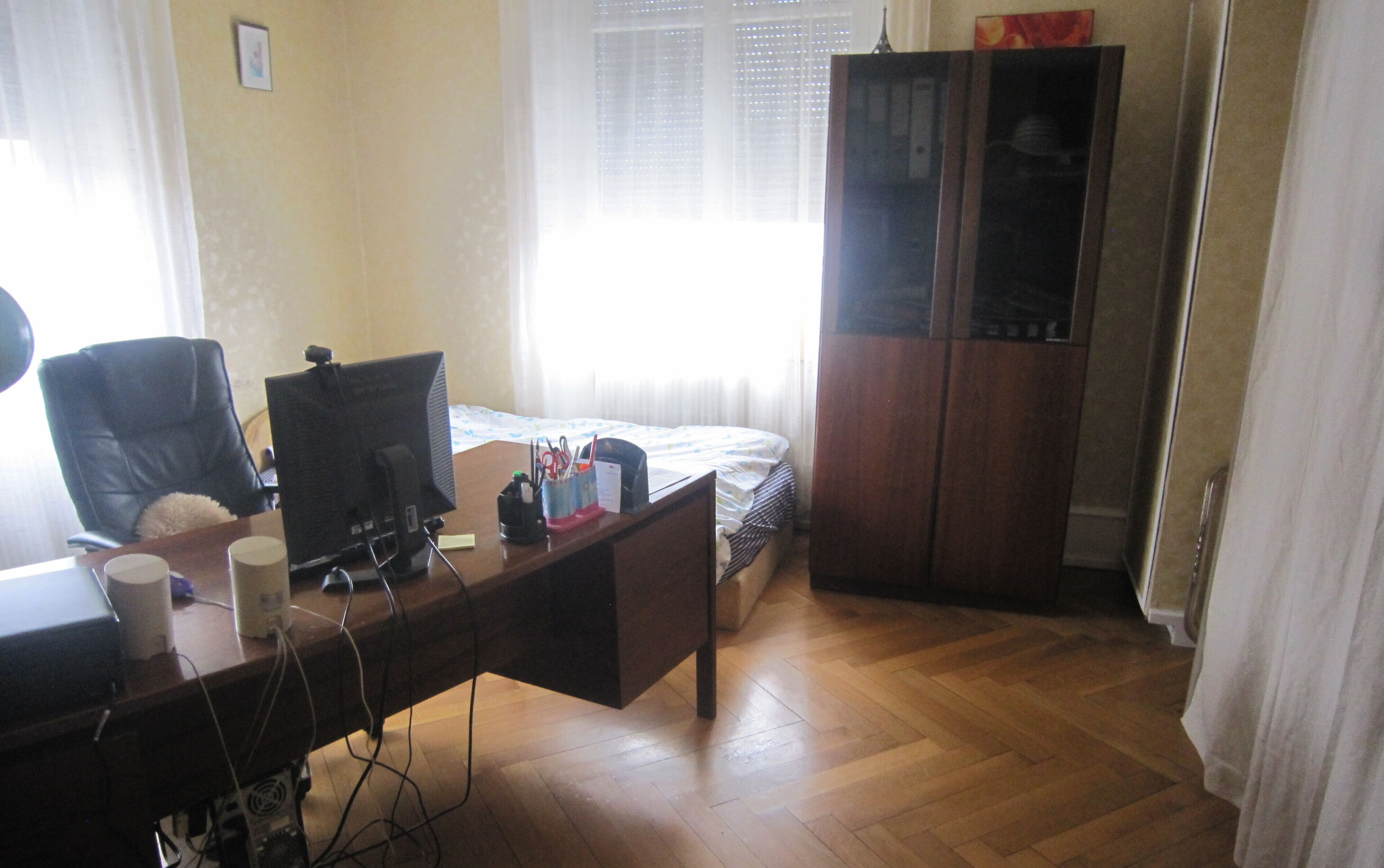 A room with a wooden desk, a computer, a chair, a bed, and a wardrobe.